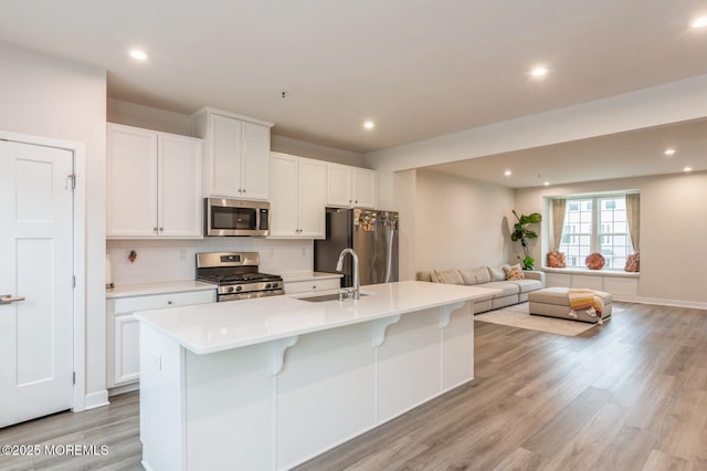 kitchen with backsplash, open floor plan, a center island with sink, appliances with stainless steel finishes, and white cabinets