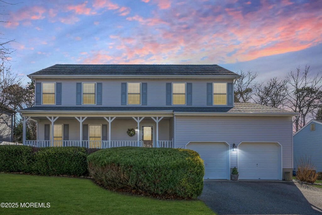 view of front of home featuring covered porch, a front lawn, aphalt driveway, and an attached garage