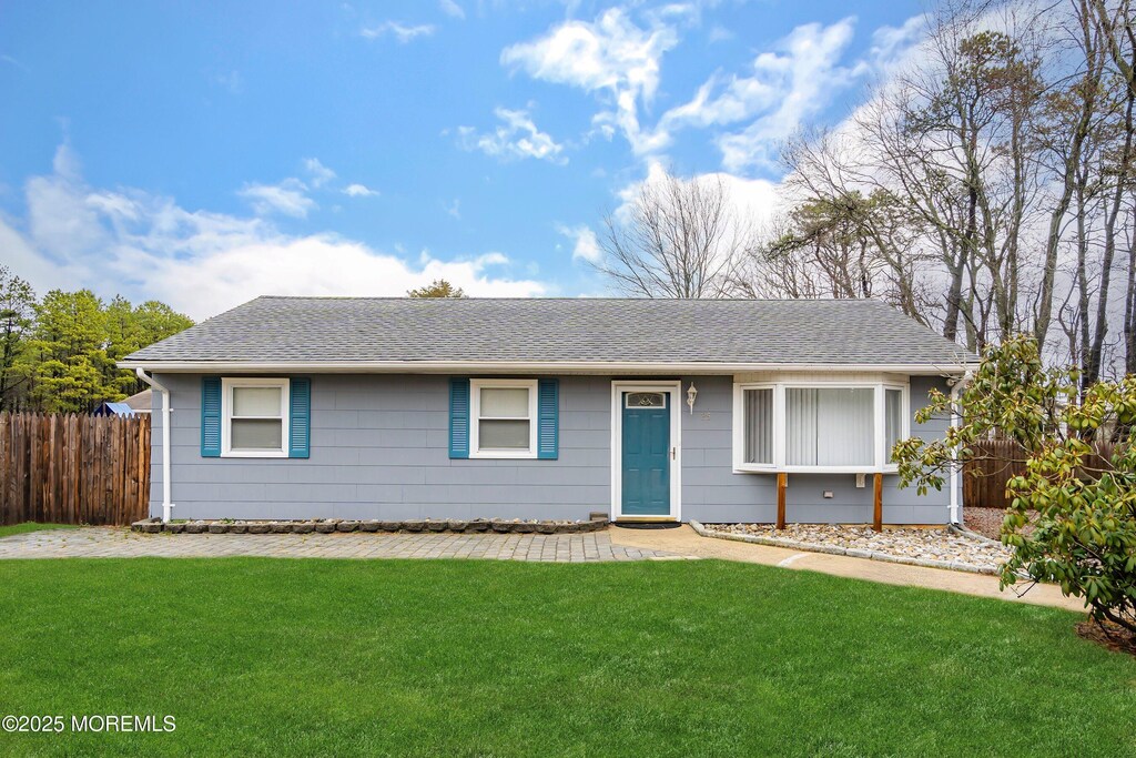 single story home featuring roof with shingles, a front yard, and fence