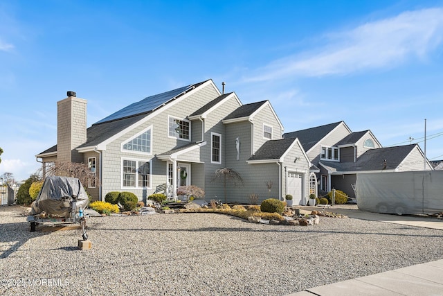 view of front of house featuring a chimney, an attached garage, and roof mounted solar panels