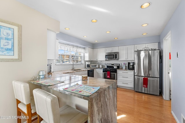 kitchen featuring a sink, stainless steel appliances, backsplash, a peninsula, and white cabinetry