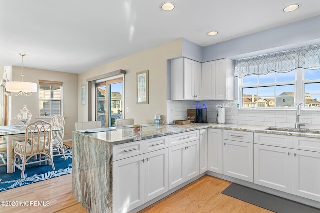 kitchen with a peninsula, white cabinets, light wood finished floors, and a sink
