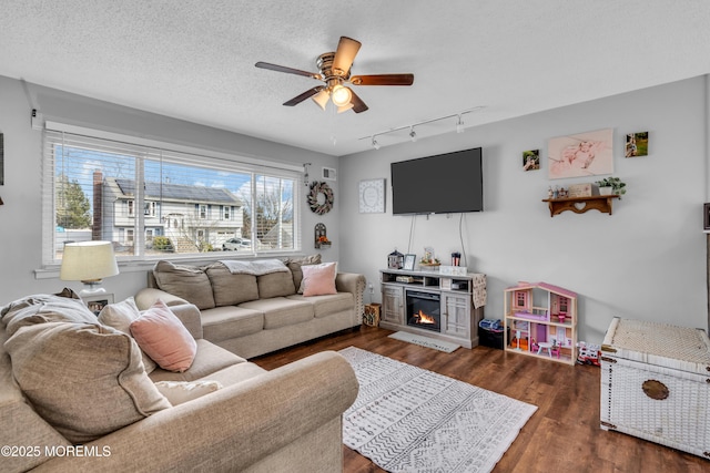 living room featuring dark wood-style flooring, a textured ceiling, ceiling fan, track lighting, and a glass covered fireplace