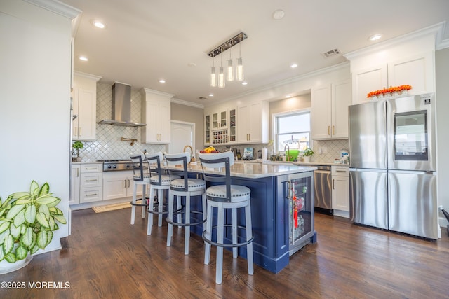 kitchen featuring white cabinets, a breakfast bar, backsplash, wall chimney exhaust hood, and appliances with stainless steel finishes