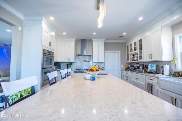 kitchen with white cabinets, glass insert cabinets, backsplash, and wall chimney range hood