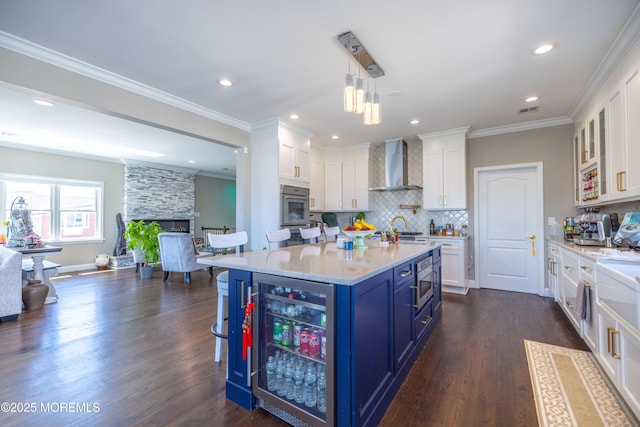 kitchen featuring blue cabinets, stainless steel appliances, beverage cooler, wall chimney range hood, and a fireplace