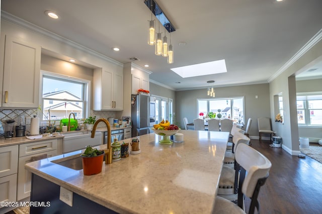 kitchen with smart refrigerator, white cabinetry, a kitchen island with sink, and a skylight
