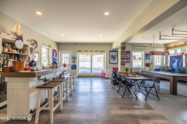 dining space with recessed lighting, plenty of natural light, a bar, and wood finished floors