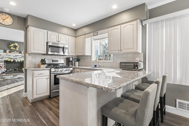 4 Whitman Rd, Morganville, NJ 07751 - kitchen featuring light stone counters, a peninsula, dark wood-style flooring, a sink, and stainless steel appliances