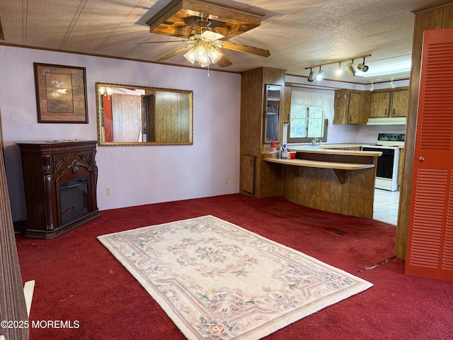 kitchen with a ceiling fan, white range with electric cooktop, a peninsula, a glass covered fireplace, and carpet flooring