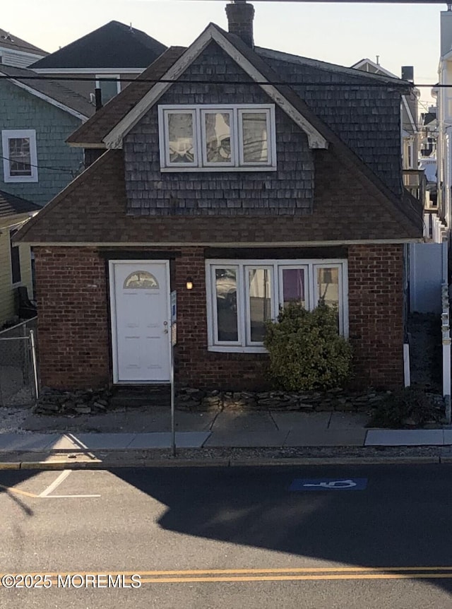 view of front of property with brick siding, a chimney, and fence