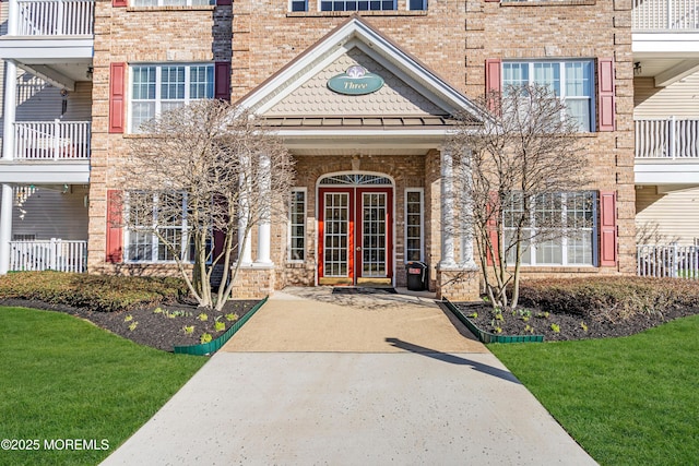 property entrance featuring french doors, brick siding, and a lawn