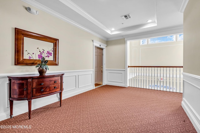 hall with a tray ceiling, recessed lighting, ornamental molding, visible vents, and a decorative wall