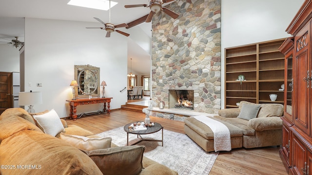 living area featuring ceiling fan, high vaulted ceiling, light wood-style flooring, beamed ceiling, and a fireplace