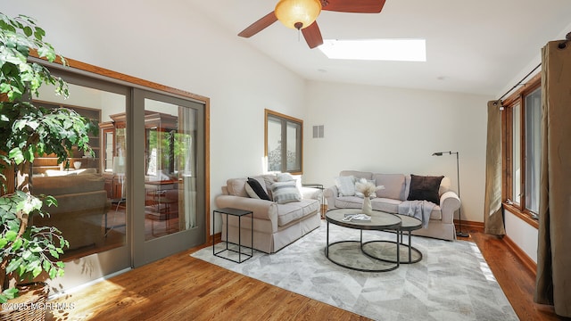 living room featuring vaulted ceiling, ceiling fan, wood finished floors, a skylight, and baseboards