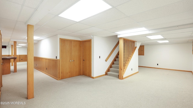 finished basement with stairway, a paneled ceiling, carpet floors, a wainscoted wall, and wooden walls