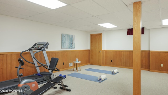 workout area featuring a wainscoted wall, a drop ceiling, carpet, and wood walls