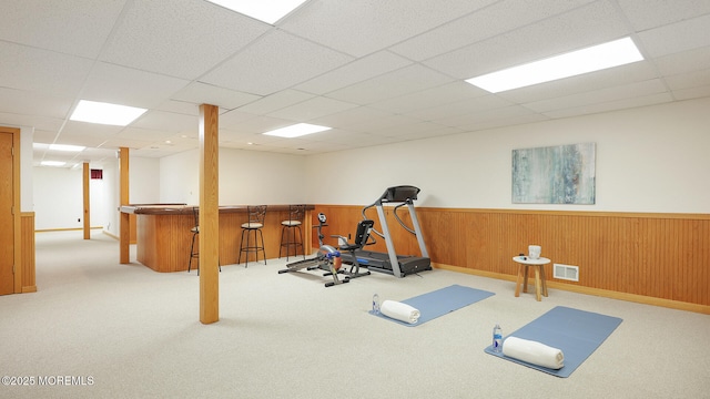 workout room with a bar, a drop ceiling, wainscoting, and carpet