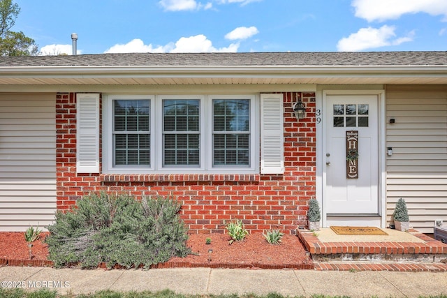 doorway to property featuring brick siding and roof with shingles