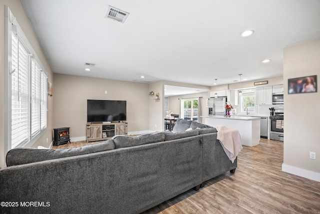 living area with a wood stove, light wood-type flooring, recessed lighting, and baseboards