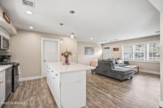 kitchen with stainless steel microwave, range with gas stovetop, wood finished floors, white cabinets, and light countertops