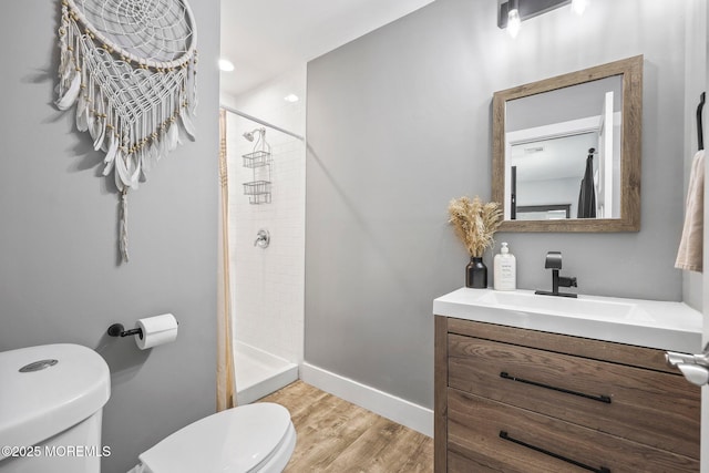 bathroom with toilet, a shower stall, wood finished floors, vanity, and baseboards