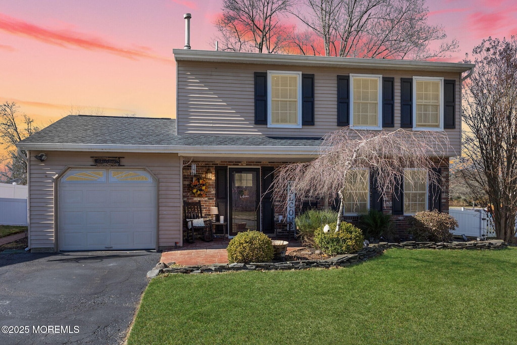 view of front facade with fence, driveway, a porch, an attached garage, and a yard