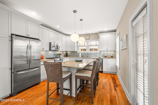 91 Cookman Ave, Ocean Grove, NJ 07756 - kitchen with stainless steel appliances, light countertops, a breakfast bar area, decorative backsplash, and light wood-type flooring