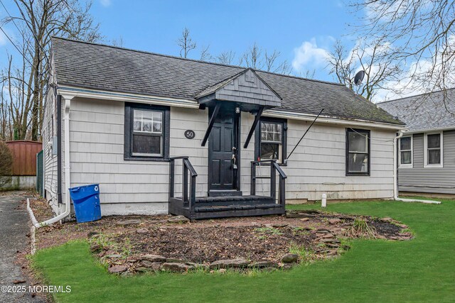 bungalow-style home with a front lawn, fence, and roof with shingles