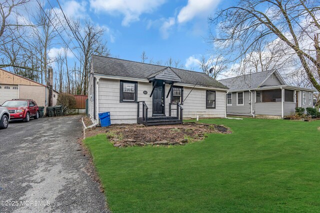 bungalow-style house featuring aphalt driveway, roof with shingles, and a front yard