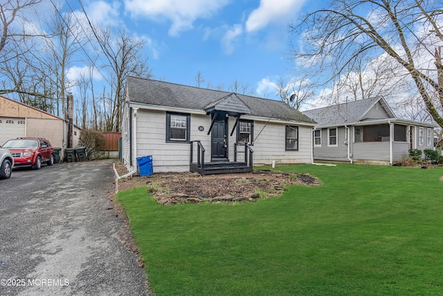 bungalow-style house featuring aphalt driveway, roof with shingles, and a front yard