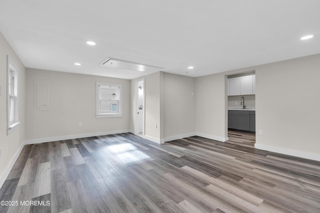 unfurnished living room featuring wood finished floors, baseboards, attic access, recessed lighting, and a sink