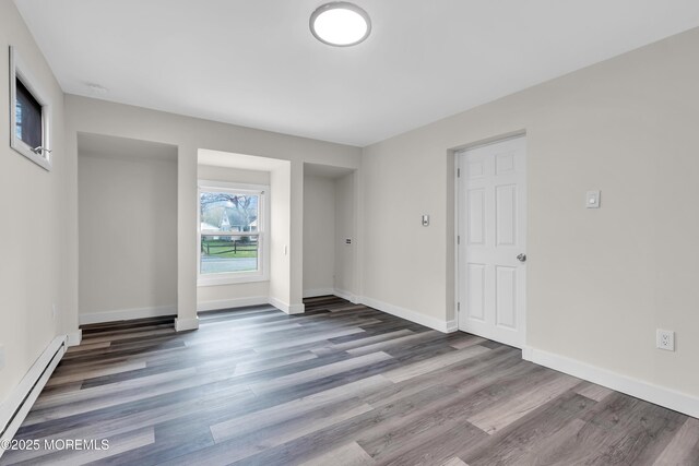 spare room featuring a baseboard heating unit, baseboards, and wood finished floors