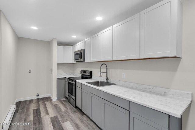 kitchen featuring a baseboard radiator, gray cabinets, appliances with stainless steel finishes, light wood-style floors, and a sink