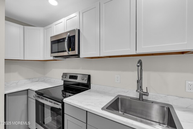 kitchen with a sink, light stone counters, appliances with stainless steel finishes, and white cabinets