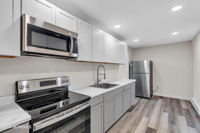 kitchen with light stone countertops, recessed lighting, light wood-style floors, stainless steel appliances, and a sink