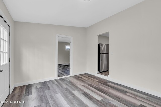 empty room with a baseboard heating unit, baseboards, and wood finished floors