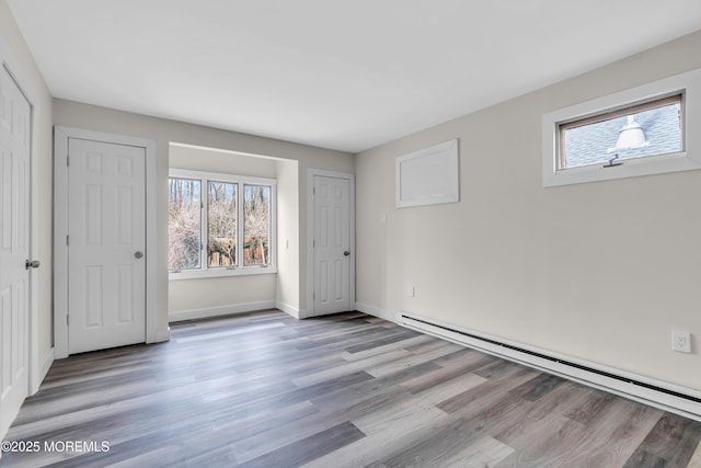 unfurnished bedroom with multiple windows, baseboards, a baseboard heating unit, and light wood-style floors