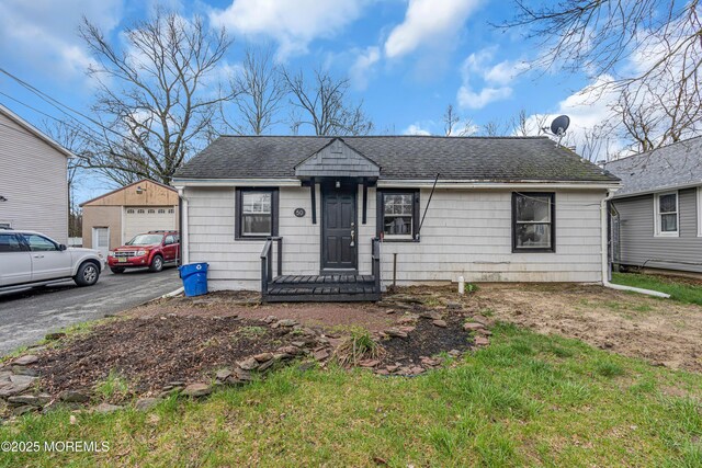 view of front of house featuring an outbuilding, a garage, roof with shingles, and aphalt driveway