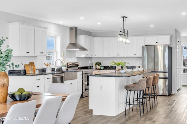 kitchen featuring stainless steel appliances, wall chimney range hood, a kitchen island, white cabinets, and recessed lighting