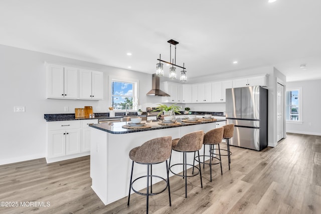 kitchen with freestanding refrigerator, wall chimney exhaust hood, dark countertops, a center island, and recessed lighting