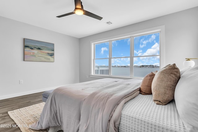 bedroom featuring wood finished floors, a water view, baseboards, and ceiling fan