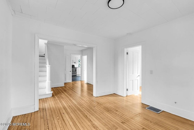 unfurnished living room featuring baseboards, stairway, light wood finished floors, and visible vents