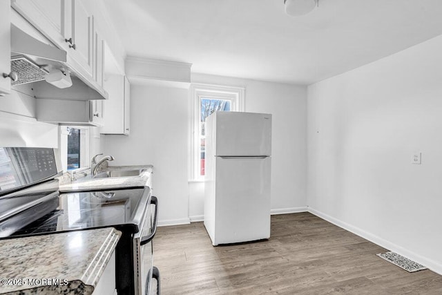 kitchen with a sink, freestanding refrigerator, visible vents, under cabinet range hood, and white cabinetry