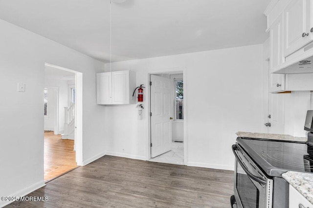 kitchen featuring baseboards, stainless steel electric range oven, white cabinets, and wood finished floors