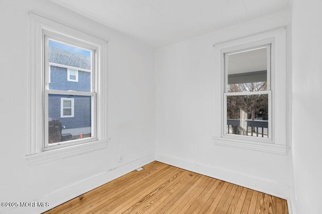 spare room featuring light wood finished floors, ornamental molding, and baseboards