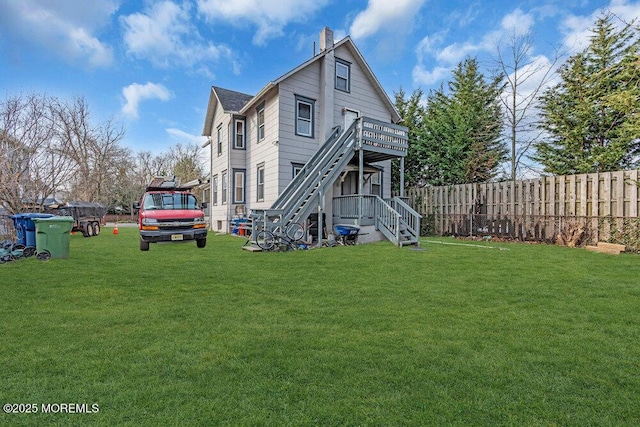 rear view of house featuring a deck, fence, stairway, a chimney, and a lawn