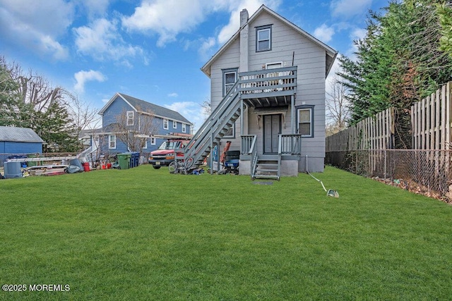 rear view of house featuring a yard, a chimney, stairway, and fence