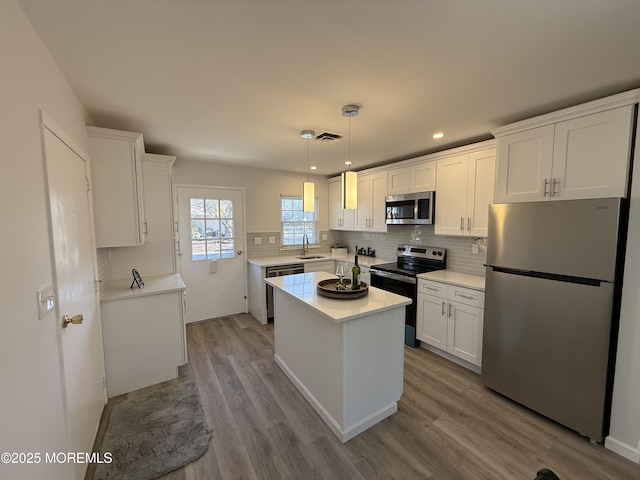 kitchen with a sink, wood finished floors, white cabinetry, appliances with stainless steel finishes, and light countertops