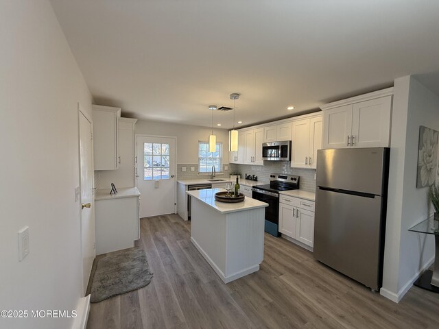 kitchen featuring wood finished floors, white cabinetry, appliances with stainless steel finishes, light countertops, and decorative backsplash